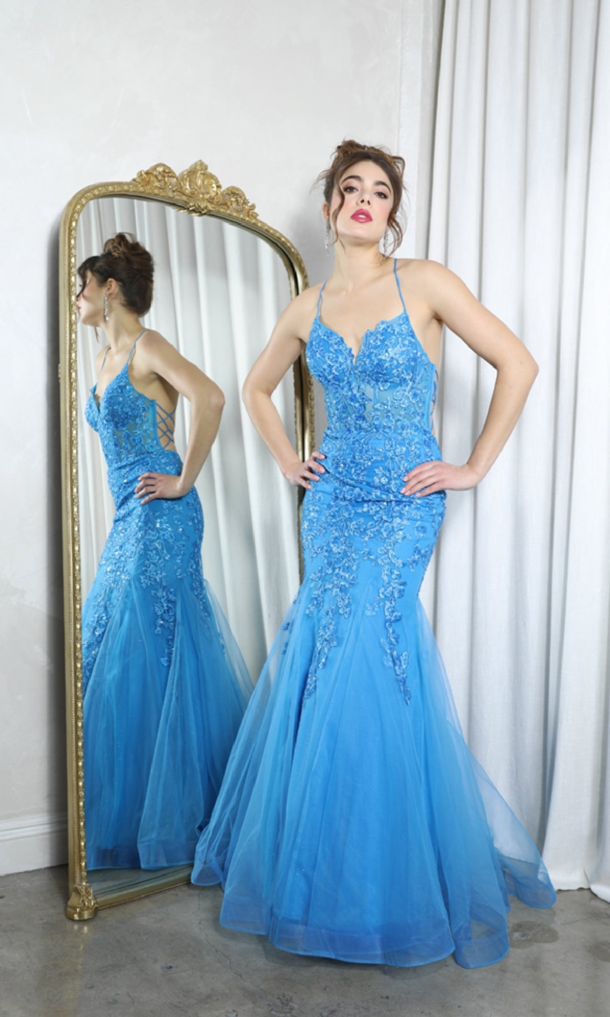 A woman in the Sequin-Floral Long Mermaid Prom Dress Eureka 9696 stands with hands on hips before a tall ornate mirror, her elegant reflection visible.